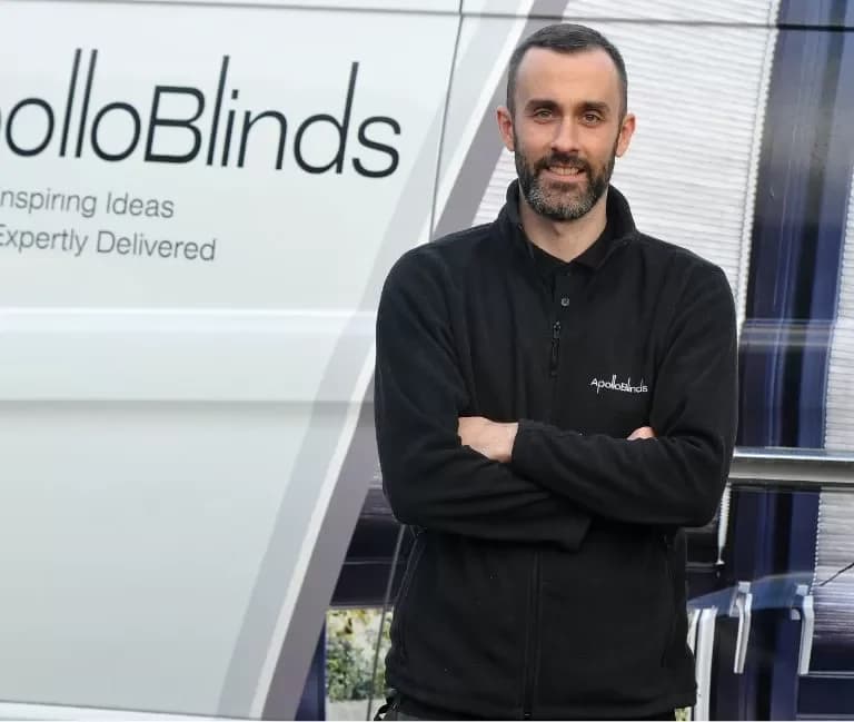 Apollo Blinds franchisee in branded fleece standing beside the company's signature 'Inspiring Ideas Expertly Delivered' service van