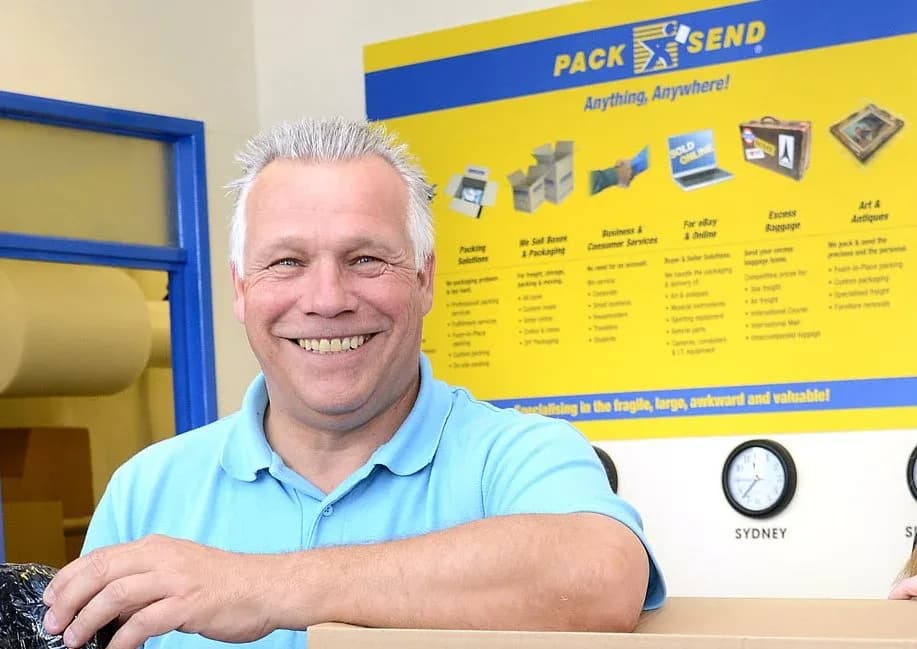 PACK & SEND franchise owner smiling inside the store with services display board