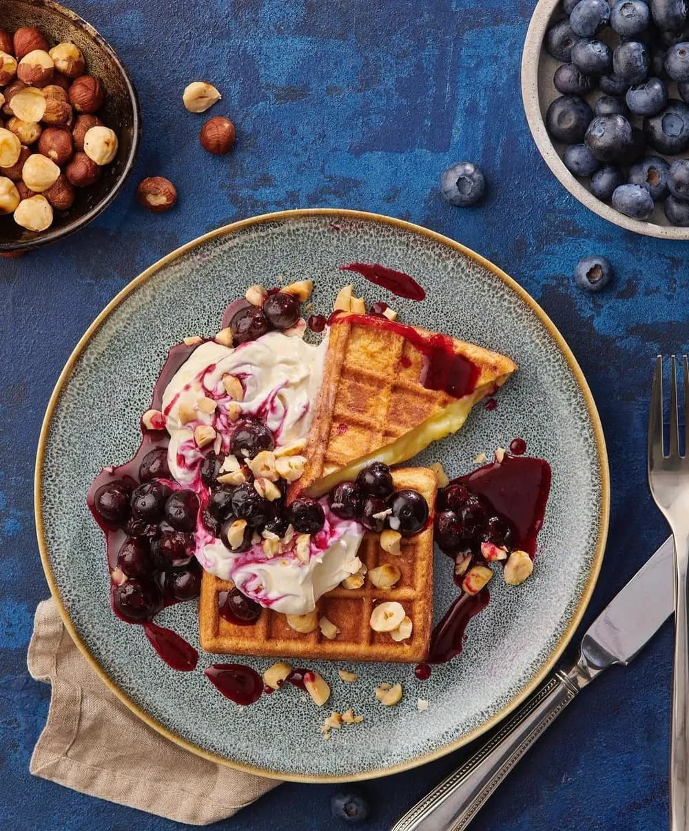 Wafflemeister waffle served on a ceramic plate with blueberry compote, hazelnuts and whipped cream