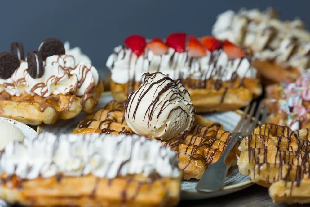 A selection of Wafflemeister waffles topped with whipped cream, chocolate drizzle, cookies and fresh strawberries