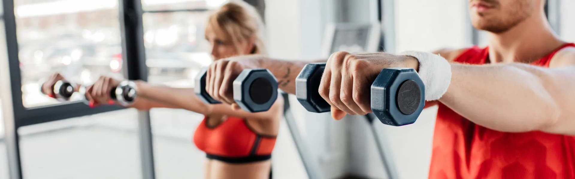 Man and woman in red sportswear lifting dumbbells during a workout in a bright gym, representing fitness franchise opportunities in the UK.