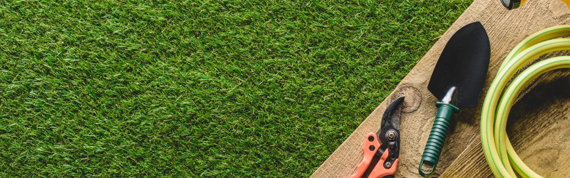 Gardening tools including pruning shears, a trowel and a hose laid on a wooden board beside lush green grass, representing gardening franchise opportunities in the UK.