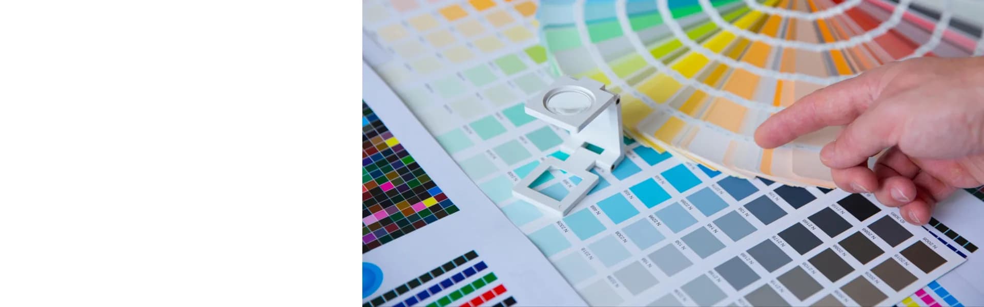 Designer selecting colours from a Pantone swatch fan with print colour charts and a magnifying loupe, representing print and sign franchise opportunities in the UK.