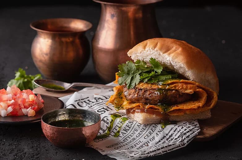 Chaiiwala Mumbai Vada Pav - Indian street-food burger with masala potato patty, fresh coriander and green and red chutneys served alongside copper serving pots