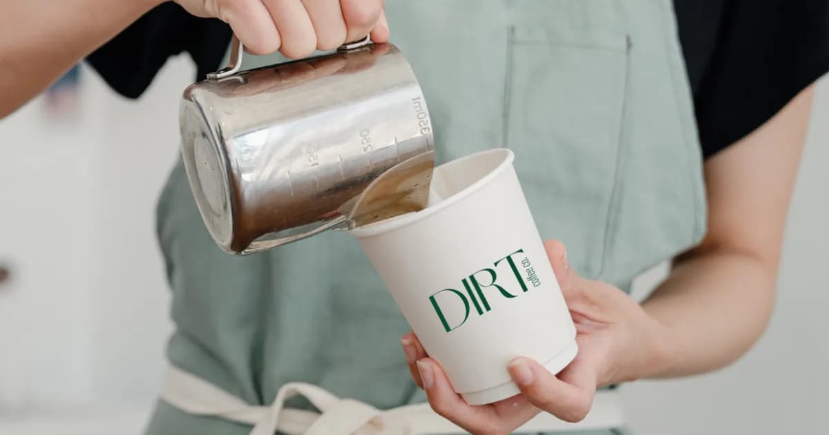 Dirt Coffee Co barista pouring a specialty latte into a branded paper cup