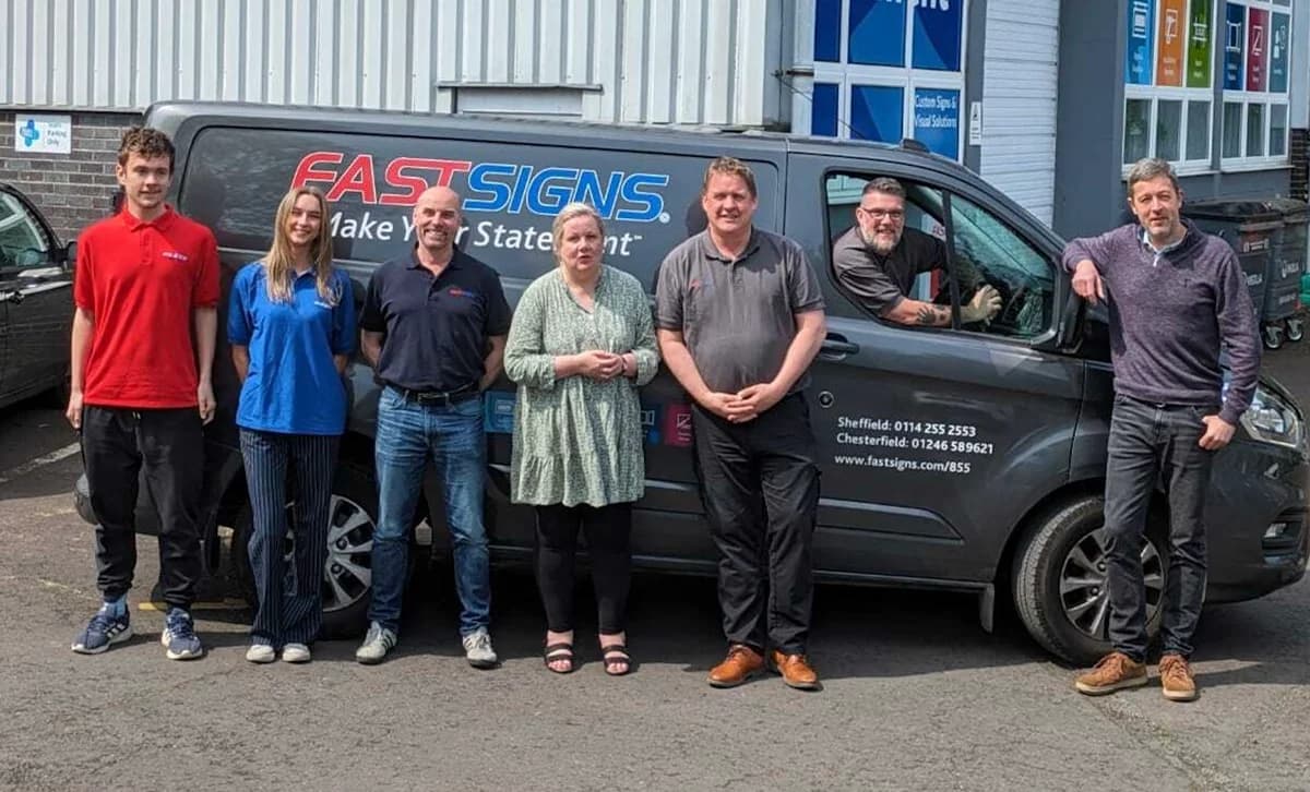 Seven-strong team of the FASTSIGNS Sheffield and Chesterfield centre lined up in front of their branded grey Ford Transit Connect van advertising the local centre's phone numbers