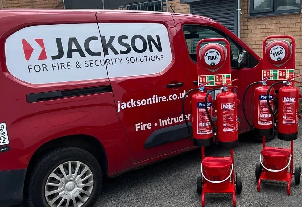 Jackson Fire & Security branded van parked alongside red Powder and Water fire extinguishers on commissioning trolleys, ready for site delivery and servicing