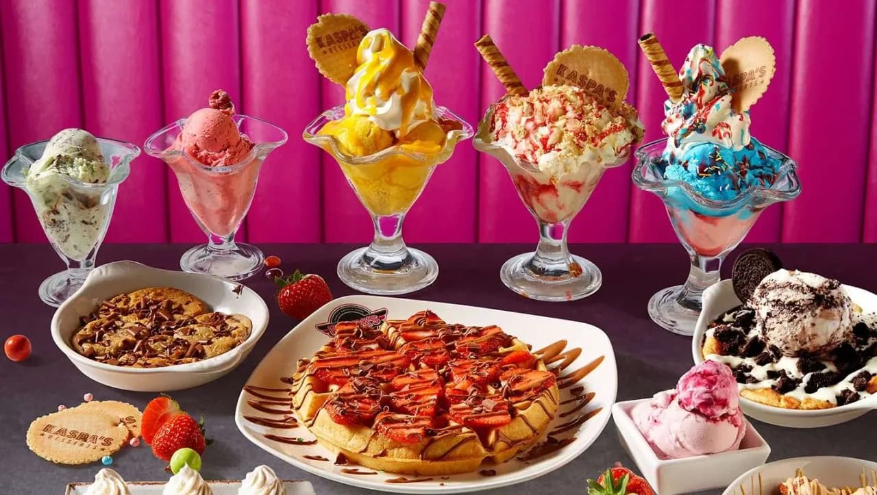 Kaspa's Desserts signature menu showcase with five colourful ice cream sundaes topped with fresh fruit, waffles with chocolate sauce, brownies and ice cream against a pink branded backdrop