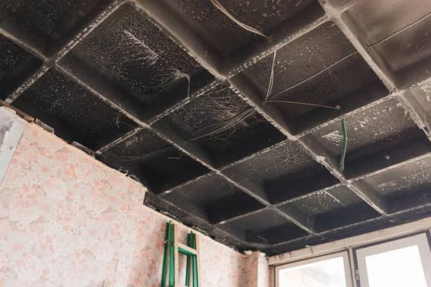Soot-blackened ceiling tiles and fire-damaged floral wallpaper inside a UK residential property after a fire - the kind of damage Rainbow Restoration franchisees recover homes from