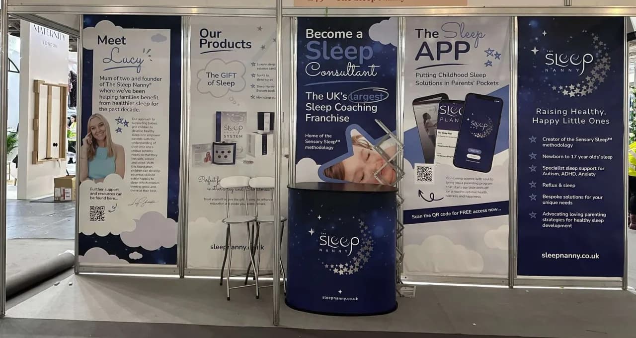The Sleep Nanny franchise exhibition stand with five branded banner panels - 'Meet Lucy' (founder profile), 'Our Products: The Gift of Sleep', 'Become a Sleep Consultant: Home of the Sensory Sleep methodology and the UK's largest Sleep Coaching Franchise', 'The Sleep APP', and a Sleep Nanny brand panel listing benefits