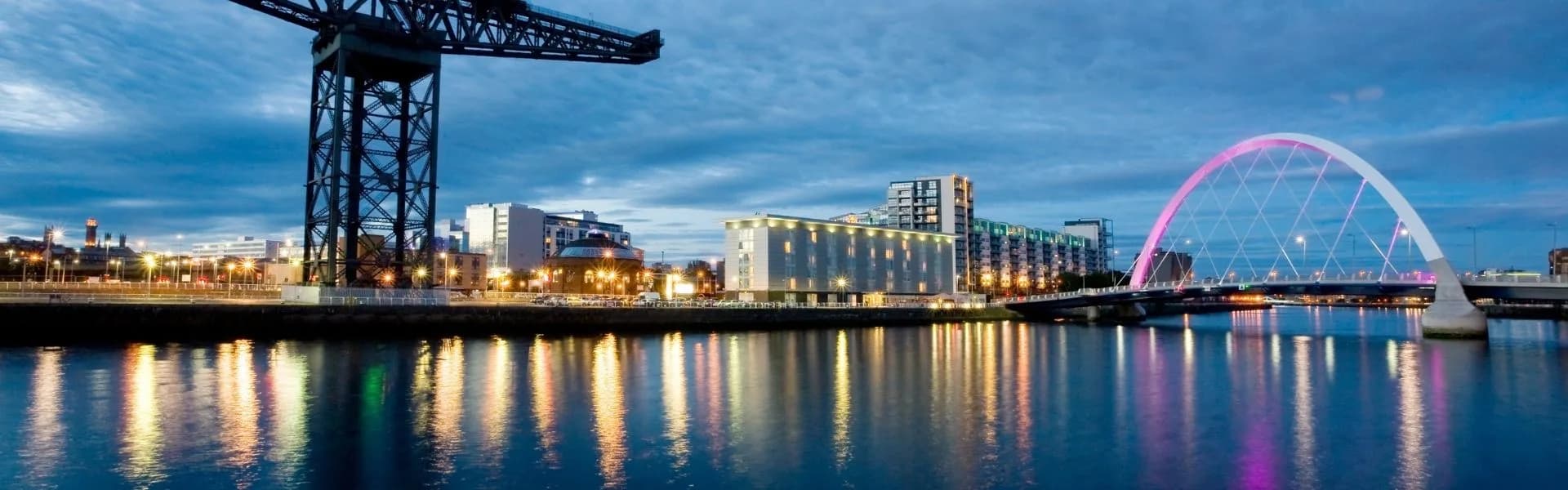 Glasgow skyline at dusk with the illuminated Clyde Arc bridge, Finnieston Crane and River Clyde reflections, representing franchise opportunities in Scotland.