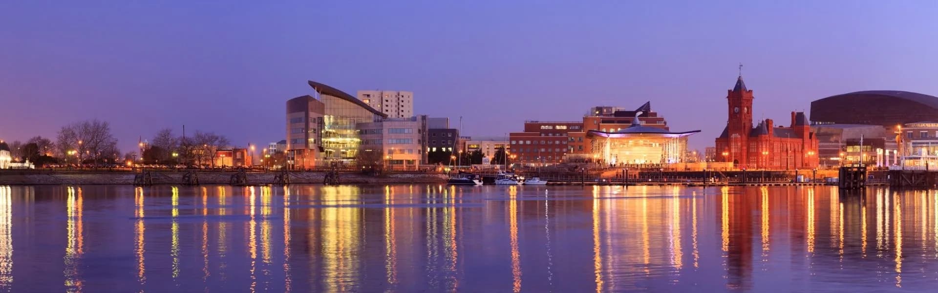 Cardiff Bay waterfront at dusk with the Pierhead Building, Wales Millennium Centre and city lights reflecting on the water, representing franchise opportunities in Wales.