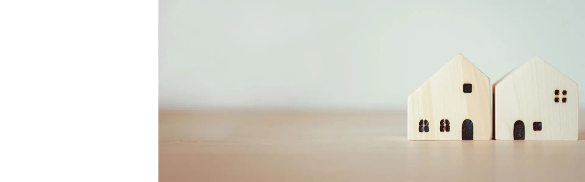 Two small wooden house models sitting side by side on a wooden surface against a soft neutral background, representing home-based franchise opportunities in the UK.