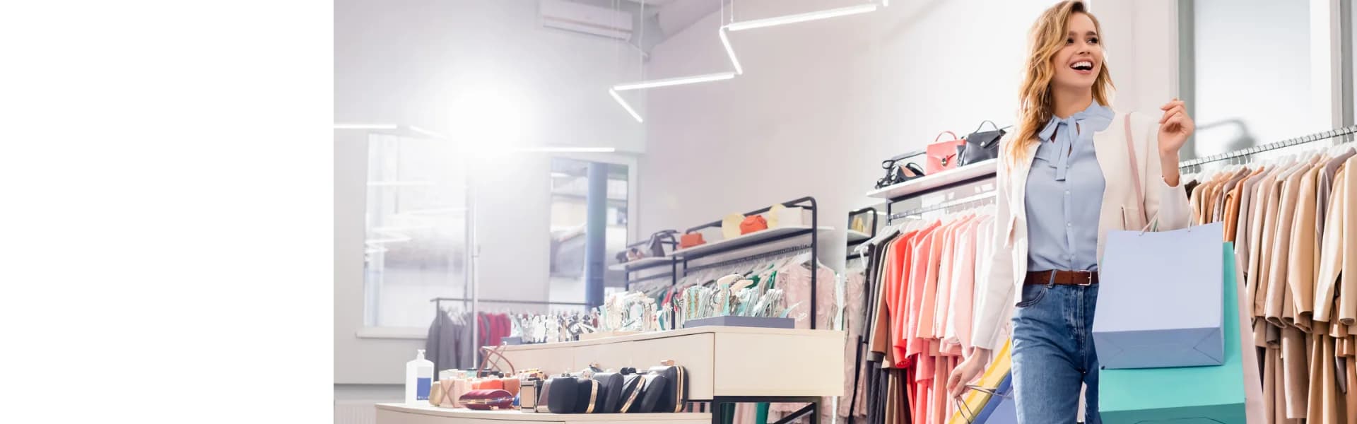 Smiling woman holding shopping bags while browsing clothing rails in a bright modern boutique, representing retail franchise opportunities in the UK.