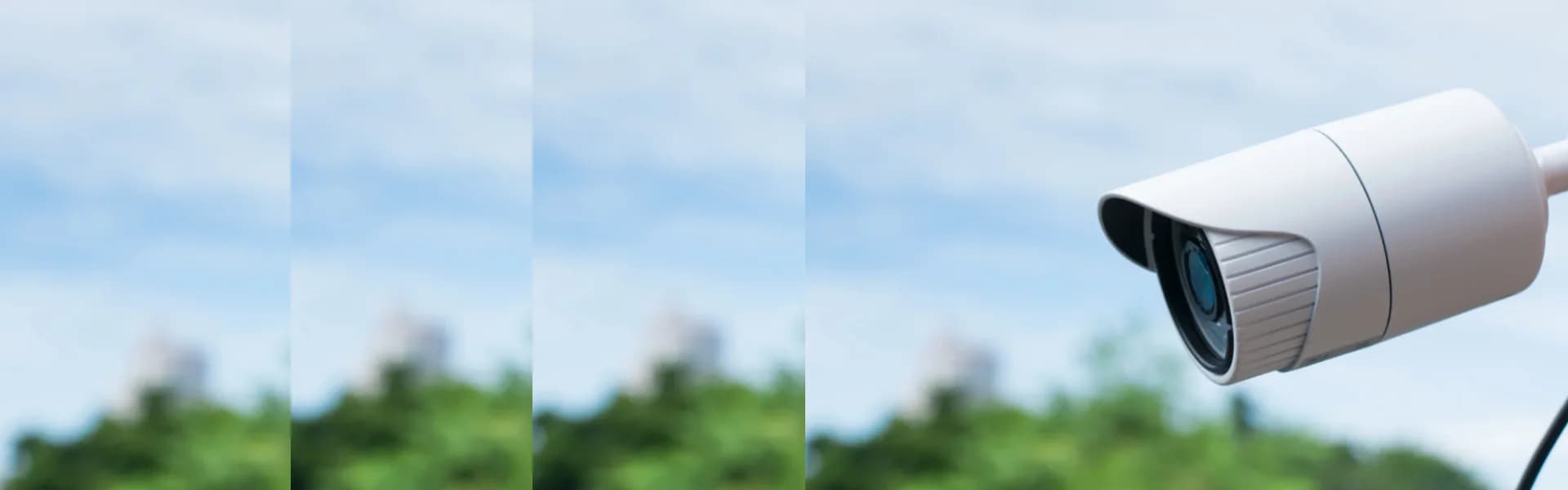 White outdoor CCTV security camera mounted against a backdrop of blue sky and green trees, representing safety and security franchise opportunities in the UK.