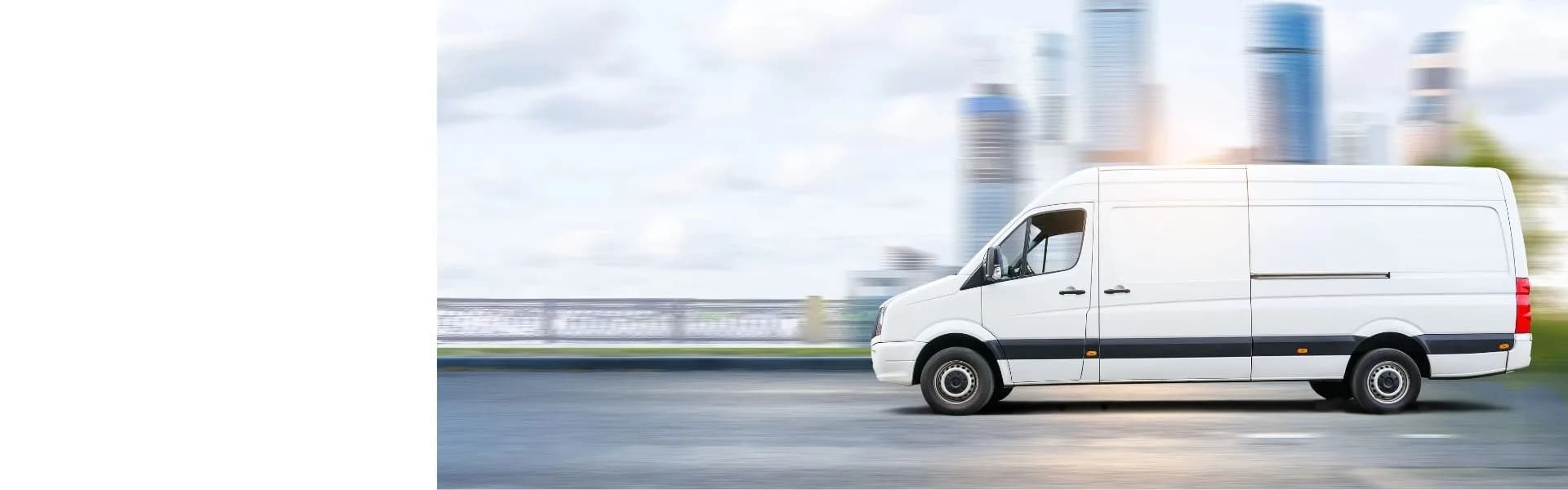 White commercial van driving along a road with a blurred city skyline in the background, representing van-based franchise opportunities in the UK.