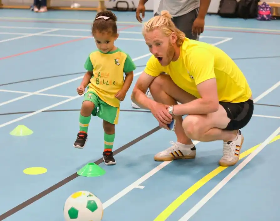 Coach supporting toddler during BabyBallers Franchise football session indoors